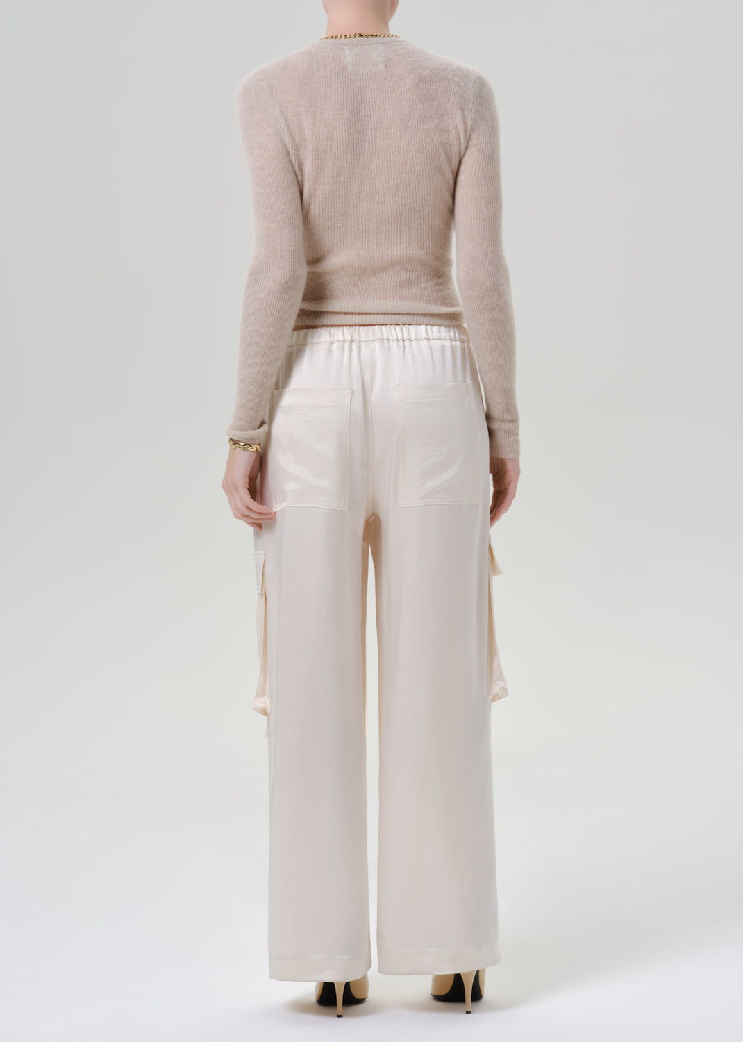 Person wearing beige long sleeve with white pants on a grey background