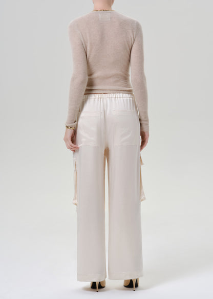 Person wearing beige long sleeve with white pants on a grey background