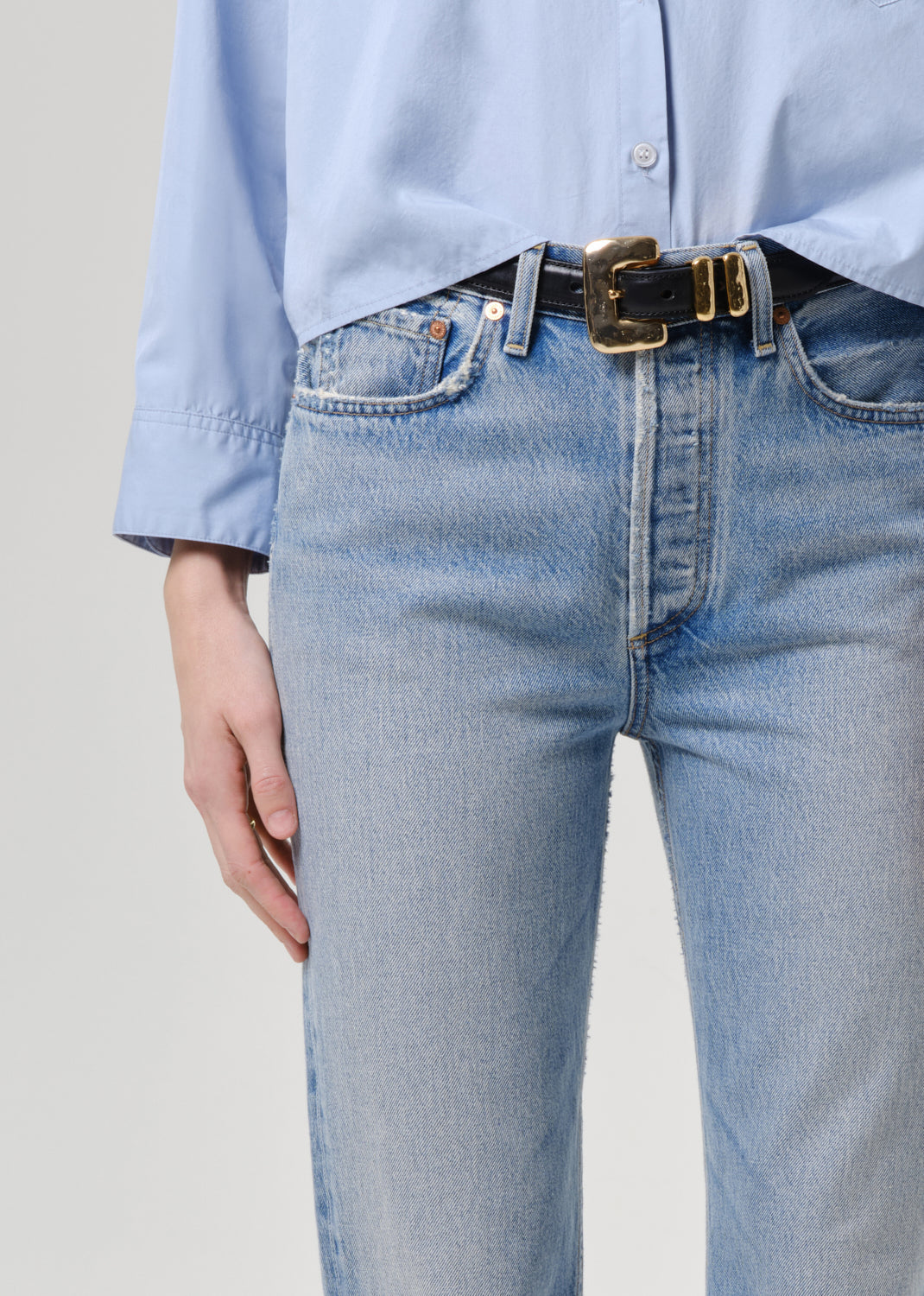 Person wearing light blue jeans and a matching shirt with a belt on a grey background