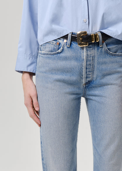 Person wearing light blue jeans and a matching shirt with a belt on a grey background