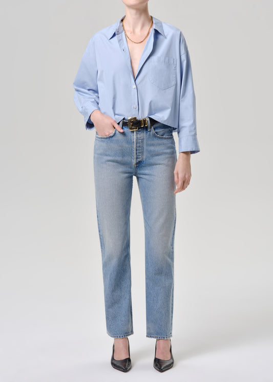 Person wearing a light blue shirt and jeans on a grey background
