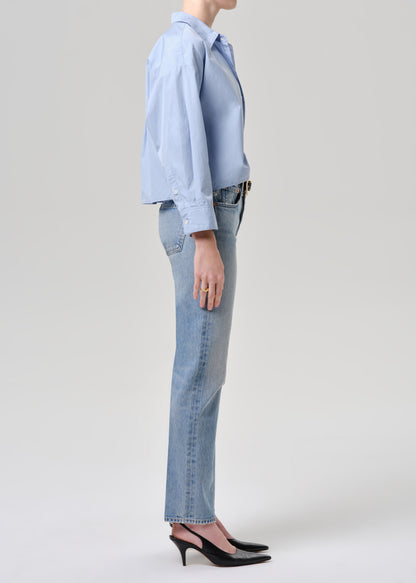Person wearing a light blue shirt and jeans on a grey background