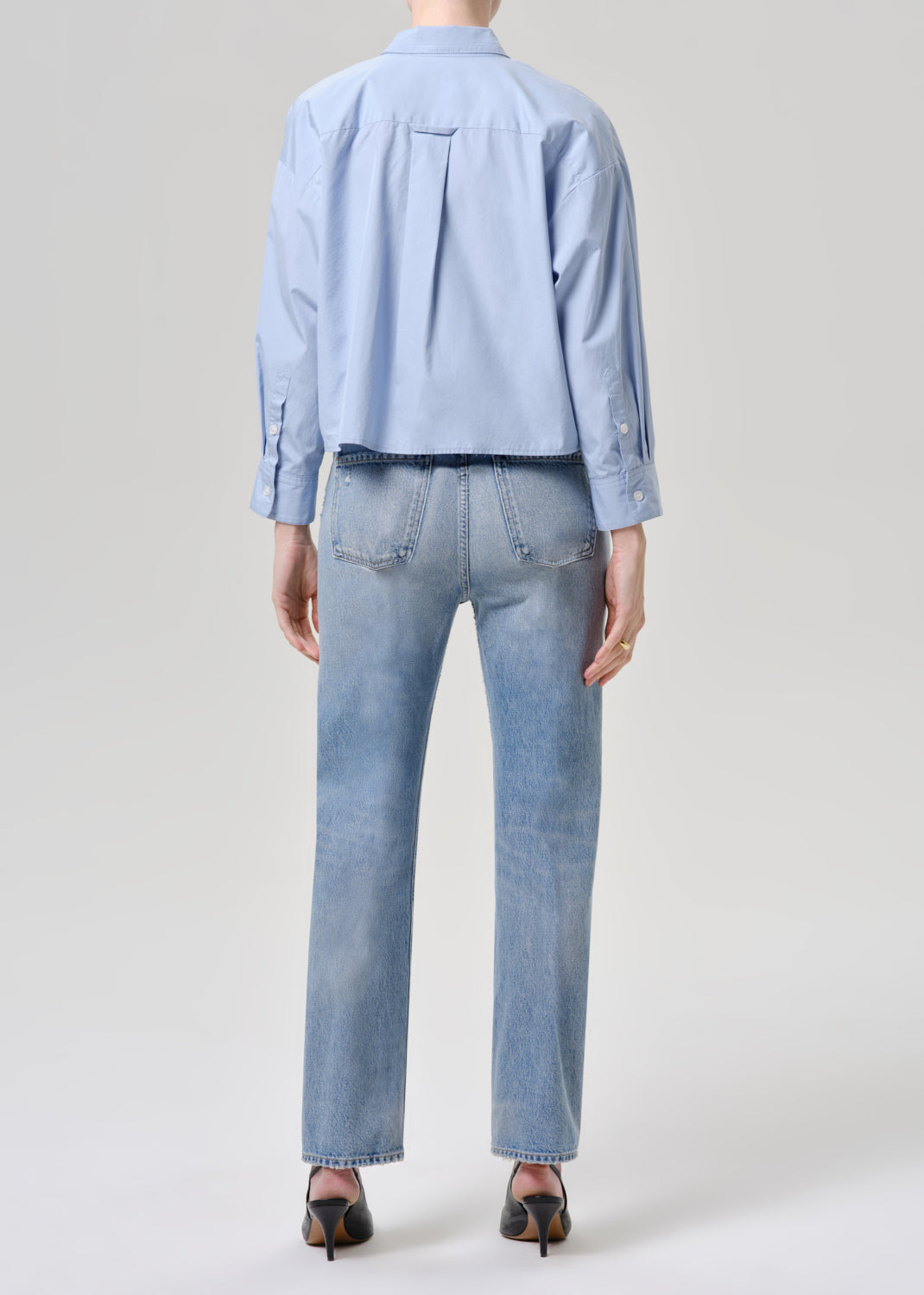 Person wearing a light blue shirt and jeans on a grey background