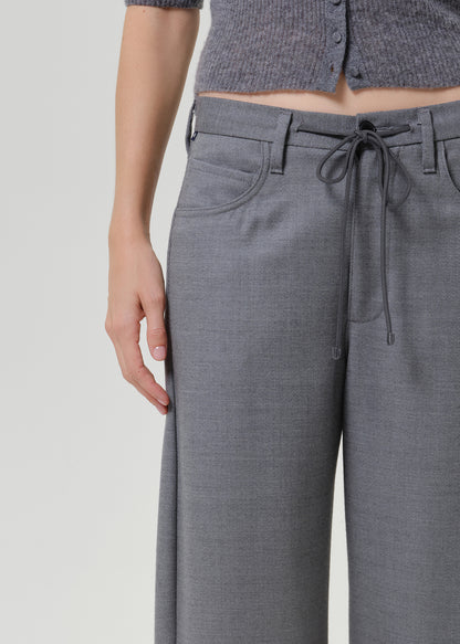Close-up of a person wearing gray wide-leg trousers with a drawstring waist, paired with a matching gray cropped top, against a light gray studio background.