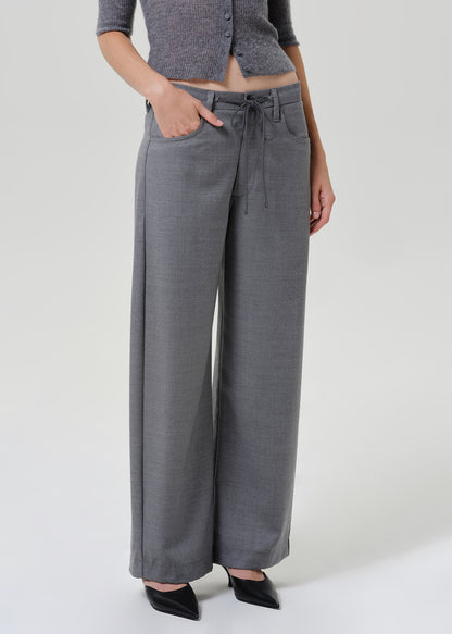 A model wearing a pair of wide-leg gray trousers with a drawstring waist, paired with a gray cropped top and black pointed shoes, photographed against a light gray studio background.
