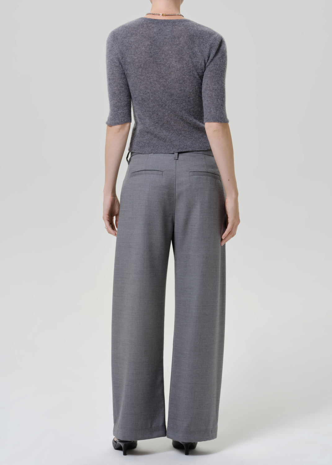A model shown from the back wearing a heathered gray three-quarter sleeve knit top and matching gray wide-leg trousers, photographed against a light gray studio background.