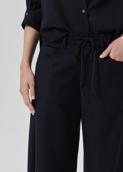 Close-up of a person wearing dark navy wide-leg trousers with a matching drawstring belt and a dark navy button-up shirt, shown against a grey background.