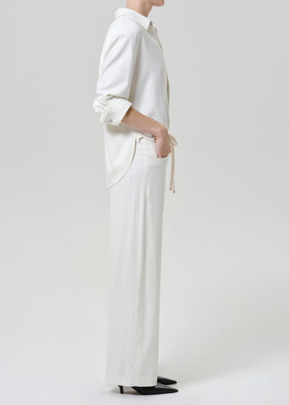 Woman wearing white wide leg pants with a white button-up shirt viewed from the side on a grey background.