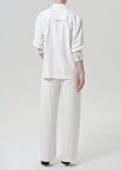 Woman wearing white wide leg pants with a white button-up shirt viewed from the back on a grey background.
