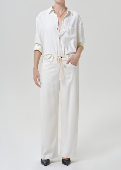 Woman wearing white wide leg pants with a white button-up shirt on a grey background.