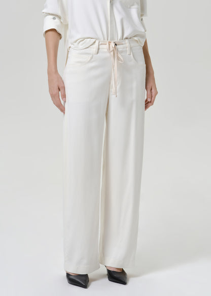 Woman wearing white wide leg pants with a white button-up shirt on a grey background.