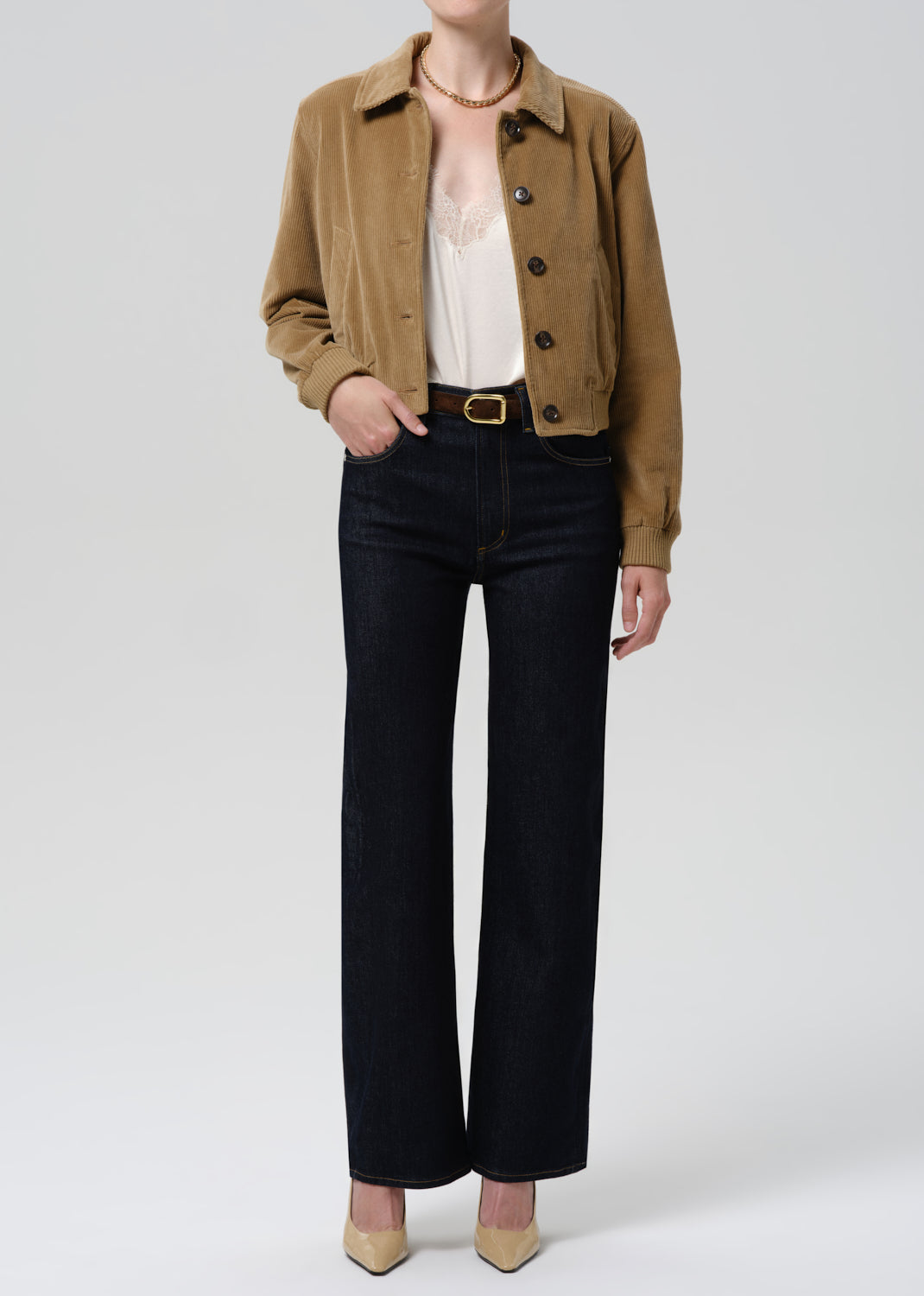 Person wearing a brown jacket and black pants on a grey background