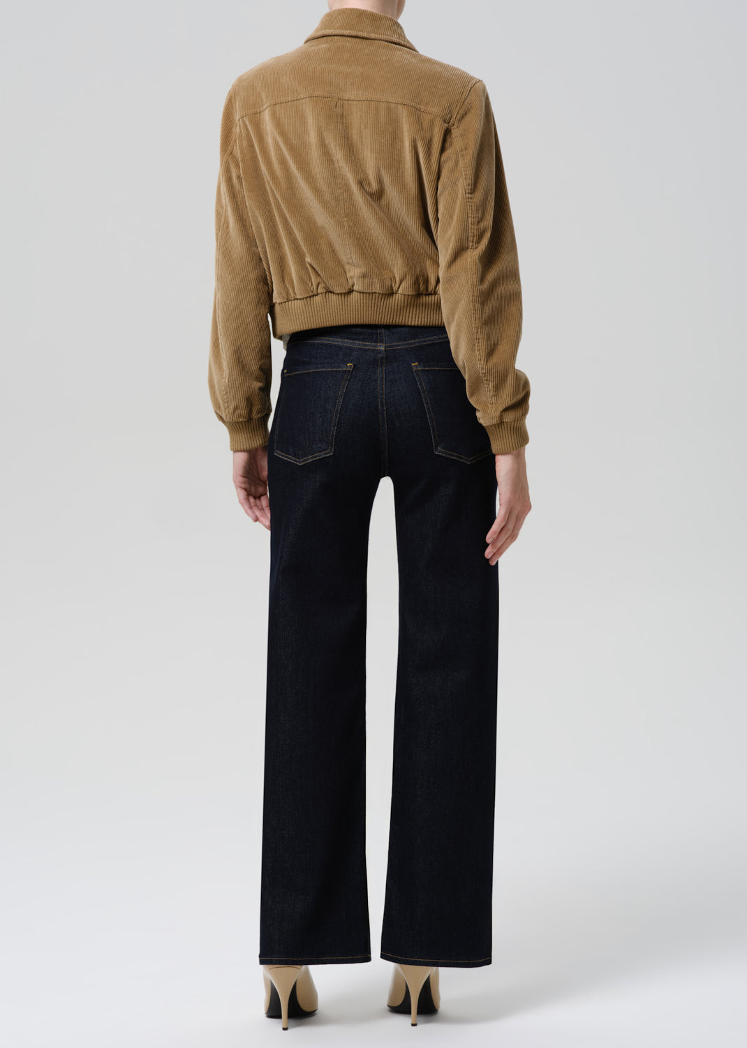 Person wearing a brown jacket and black pants on a grey background