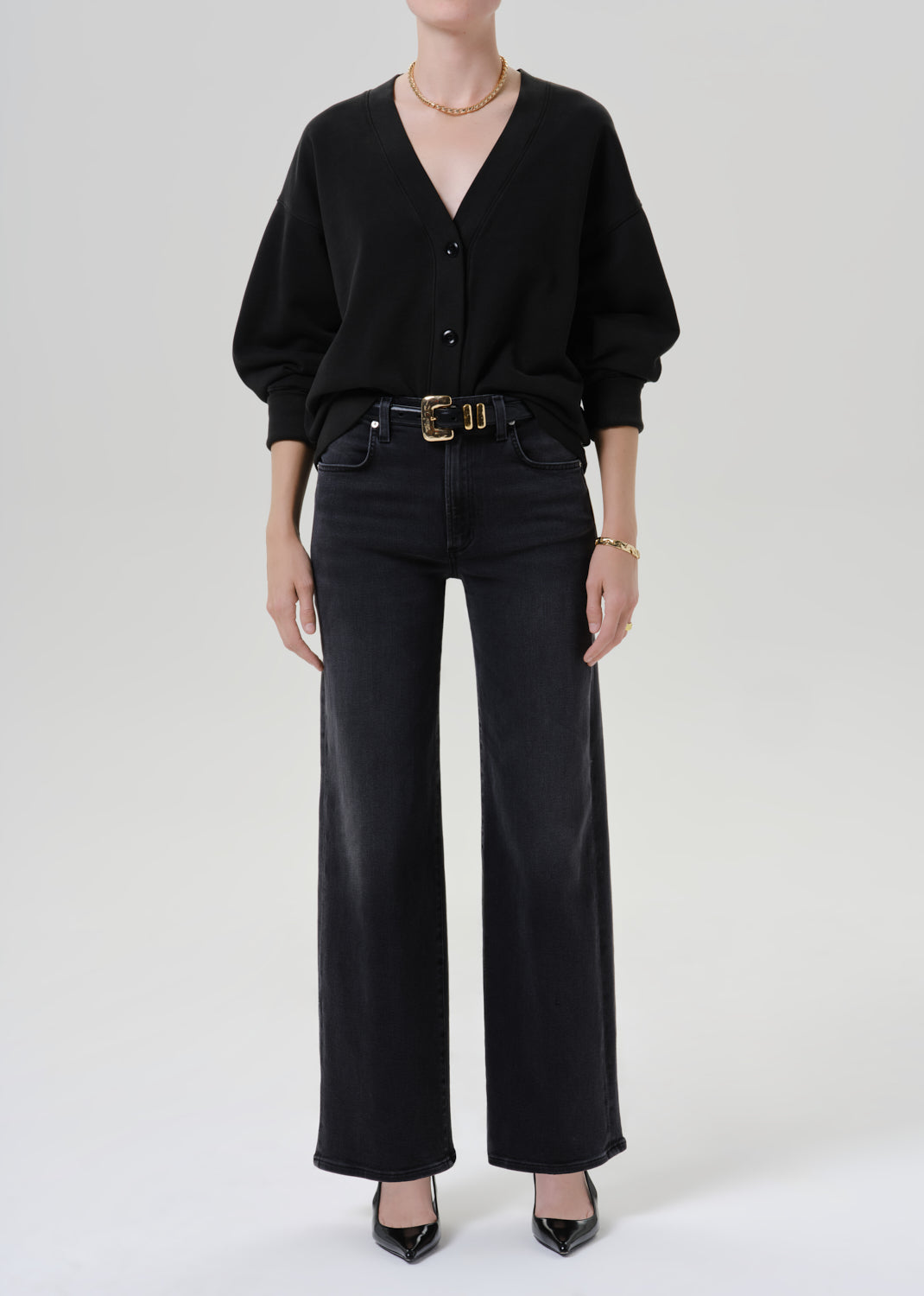 Person wearing a black cardigan and black pants on a grey background