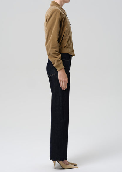 Person wearing a brown jacket and black pants on a grey background