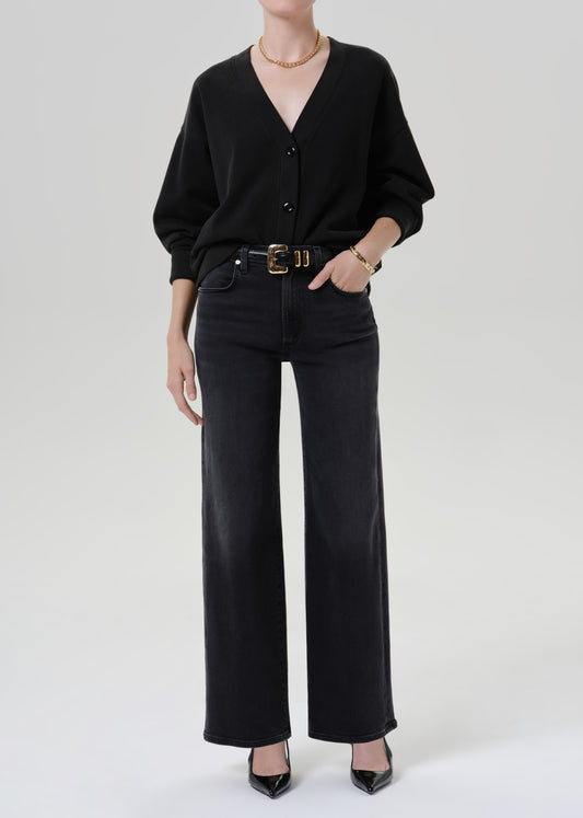 Person wearing black cardigan sweater with black pants on a grey background