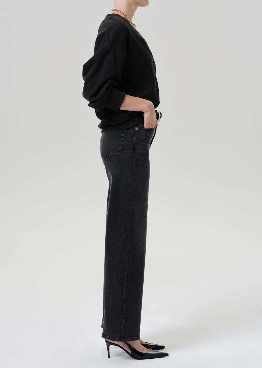 Person wearing black cardigan sweater with black pants on a grey background