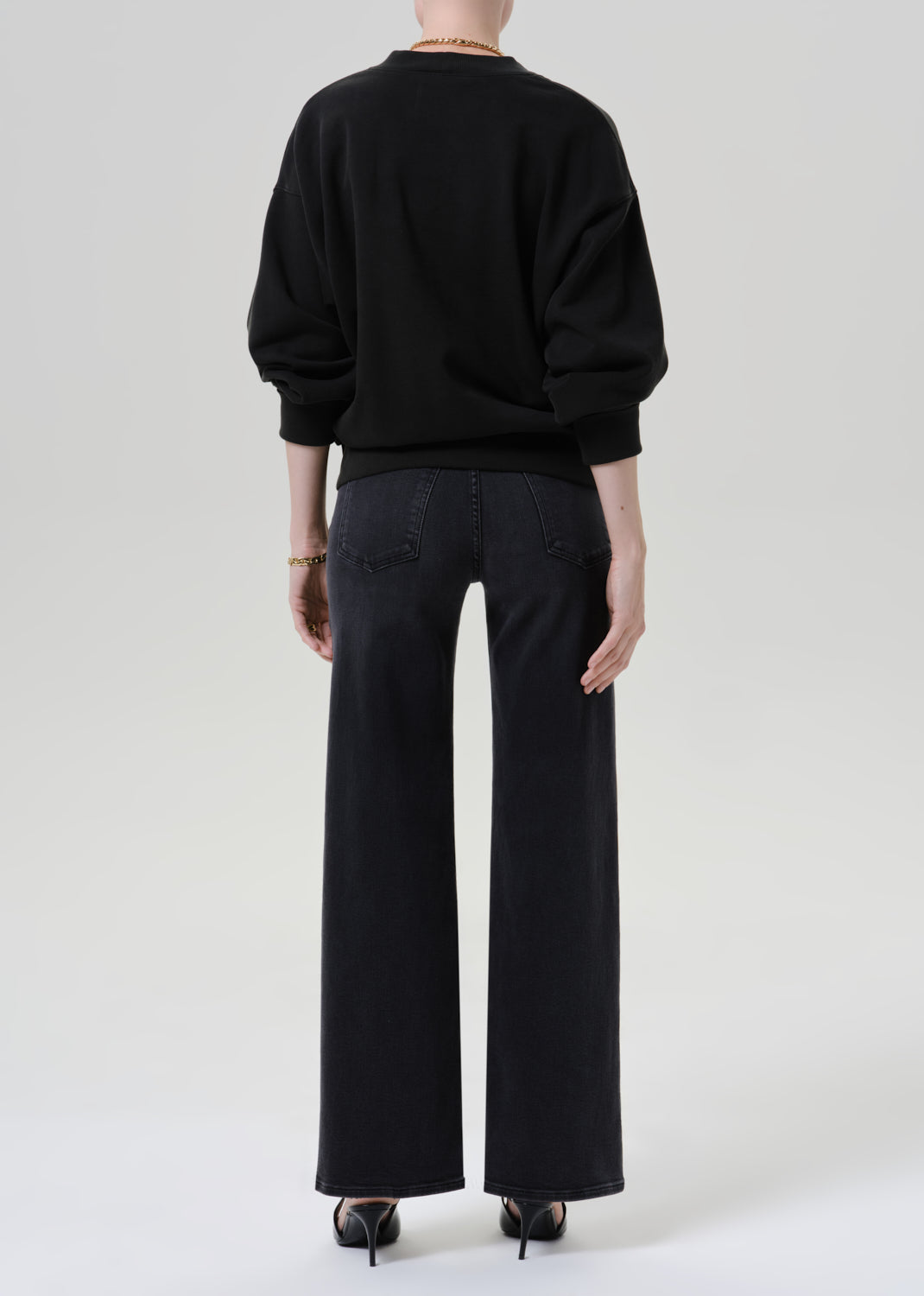 Person wearing black cardigan sweater with black pants on a grey background