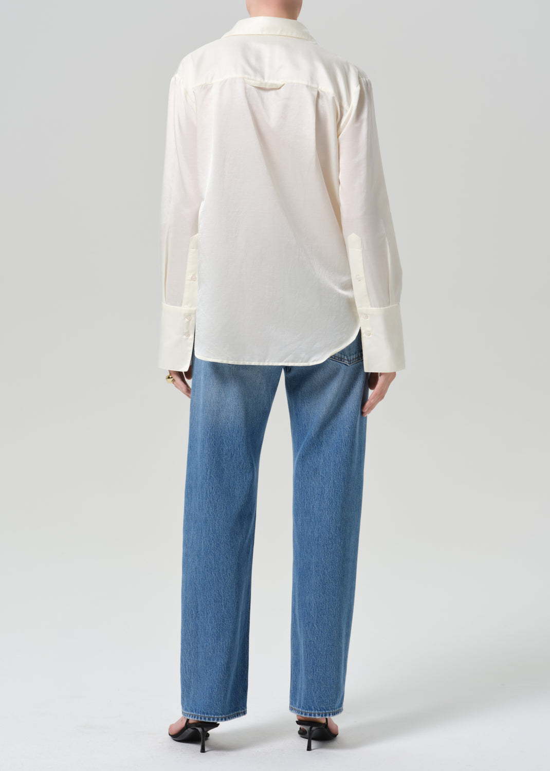 A model shown from the back wearing a white long-sleeve button-down shirt and blue jeans against a grey background.