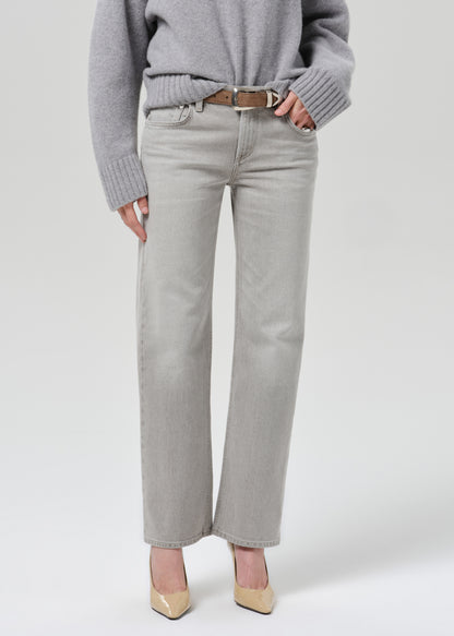 Person wearing a light grey oversized turtleneck sweater with light grey straight leg jeans on a grey background