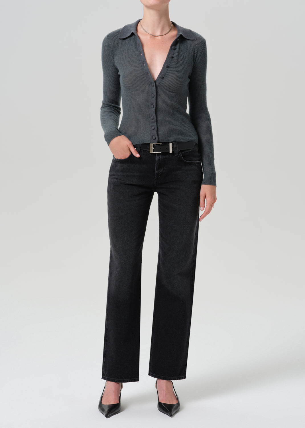 A model wearing a dark grey long-sleeve button-up knit top, black wide-leg jeans, and black pointed-toe heels, standing against a grey background.