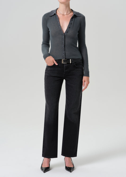 A model wearing a dark grey long-sleeve button-up knit top, black wide-leg jeans, and black pointed-toe heels, standing against a grey background.