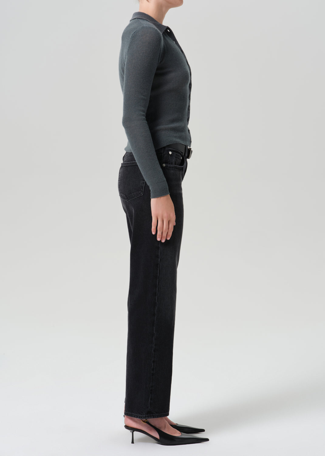 A model shown in profile wearing a dark grey long-sleeve knit top, black wide-leg jeans, and black pointed-toe mule heels against a grey background.