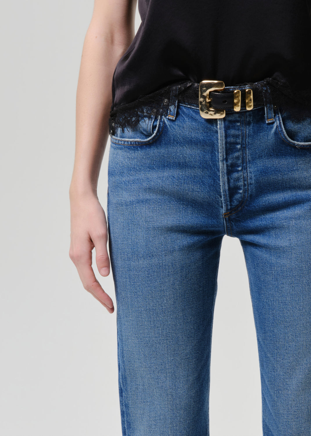 Person wearing blue jeans with a gold belt on a grey background
