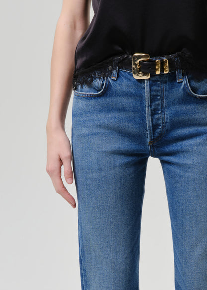 Person wearing blue jeans with a gold belt on a grey background