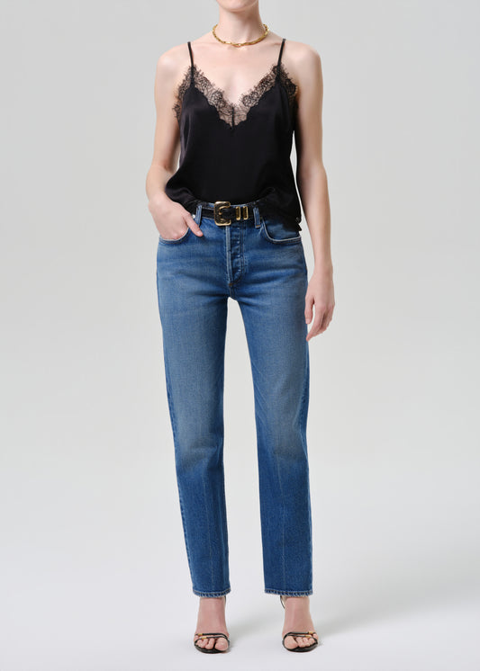 Person wearing a black lace top and blue jeans on a grey background