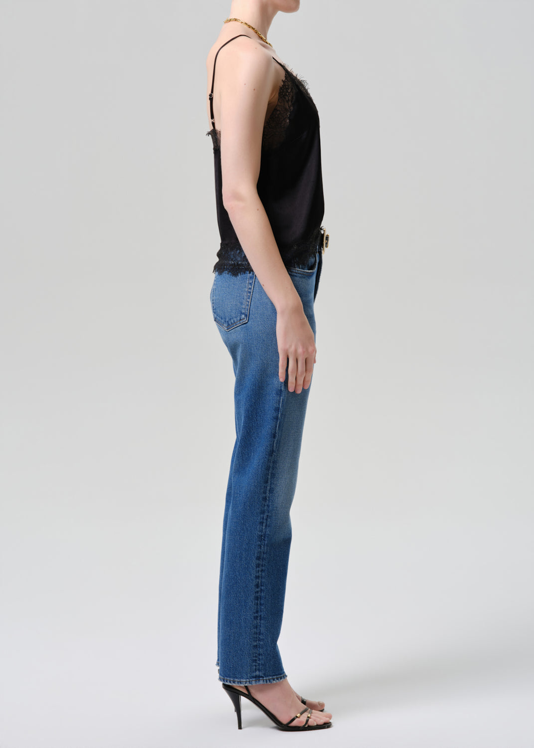 Person wearing a black sleeveless top and blue jeans on a grey background