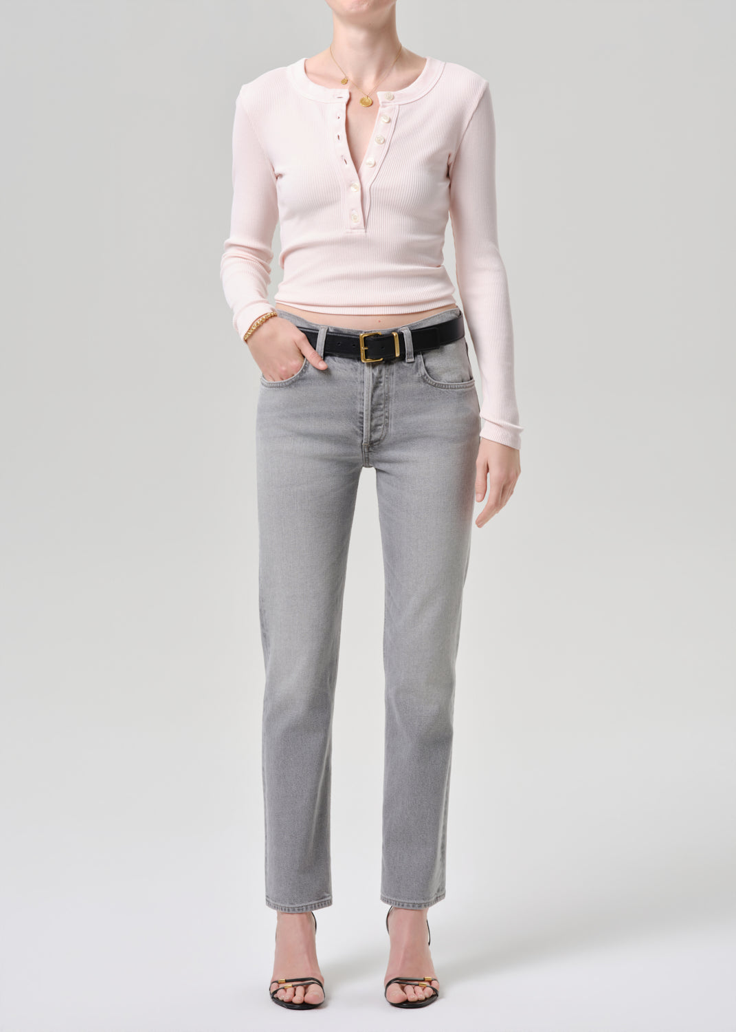 Person wearing a light pink long-sleeve shirt and grey jeans on a grey background