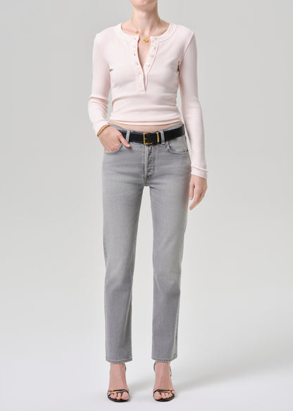 Person wearing a light pink long-sleeve shirt and grey jeans on a grey background