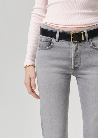 Person wearing light gray jeans with a black belt on a grey background
