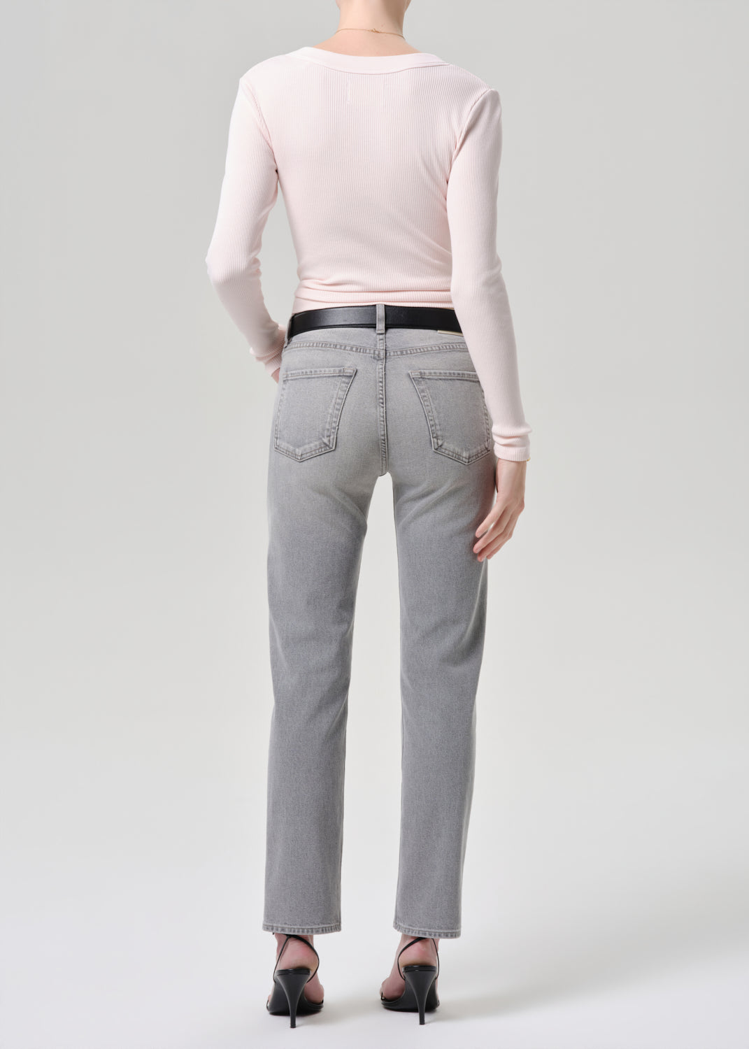Person wearing gray jeans and a light pink long-sleeve top on a grey background