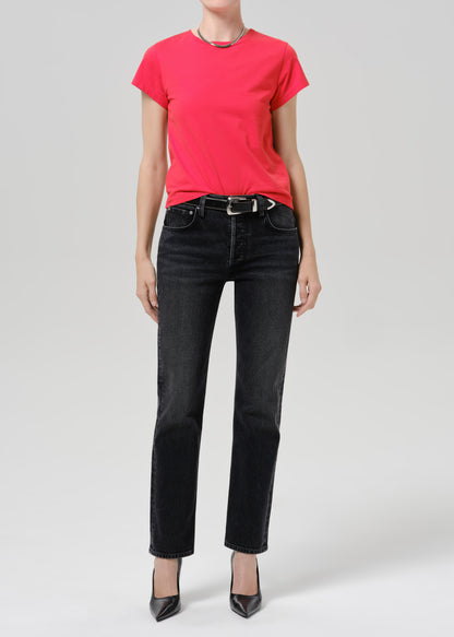 Person wearing a bright pink short sleeve crewneck tee with black straight-leg jeans and black pointed-toe heels on a grey background