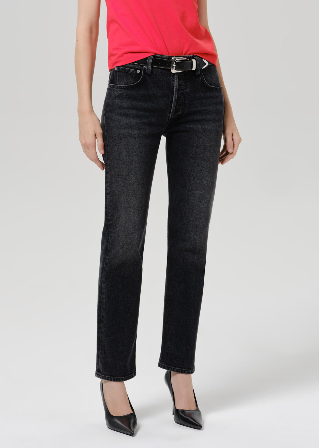 Person wearing a bright pink short sleeve crewneck tee with black straight-leg jeans and black pointed-toe heels on a grey background