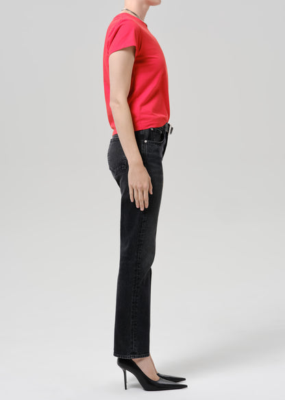 Person wearing a bright pink short sleeve crewneck tee with black straight-leg jeans viewed from the side on a grey background