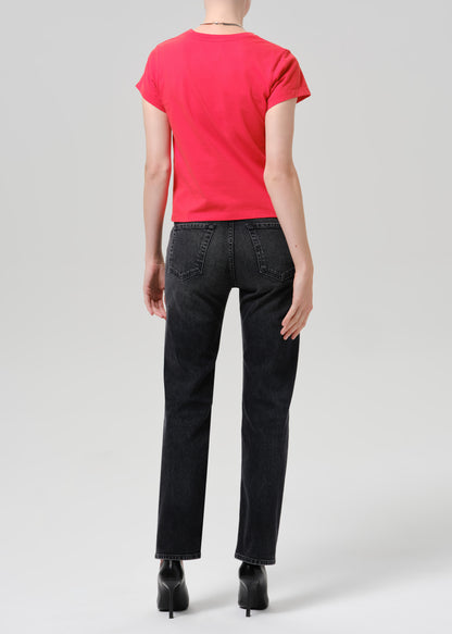Person wearing a bright pink short sleeve crewneck tee with black straight-leg jeans viewed from the back on a grey background