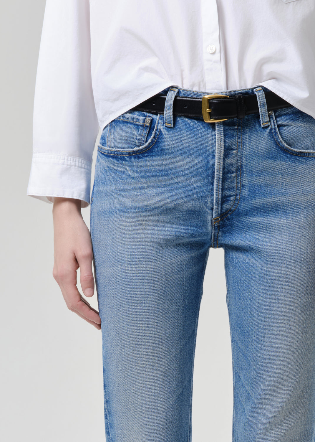 Person wearing blue jeans and a white shirt with a grey background
