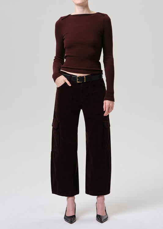 A model wearing a dark burgundy long-sleeve knit top and dark brown wide-leg velvet pants with a black belt, standing against a grey background.