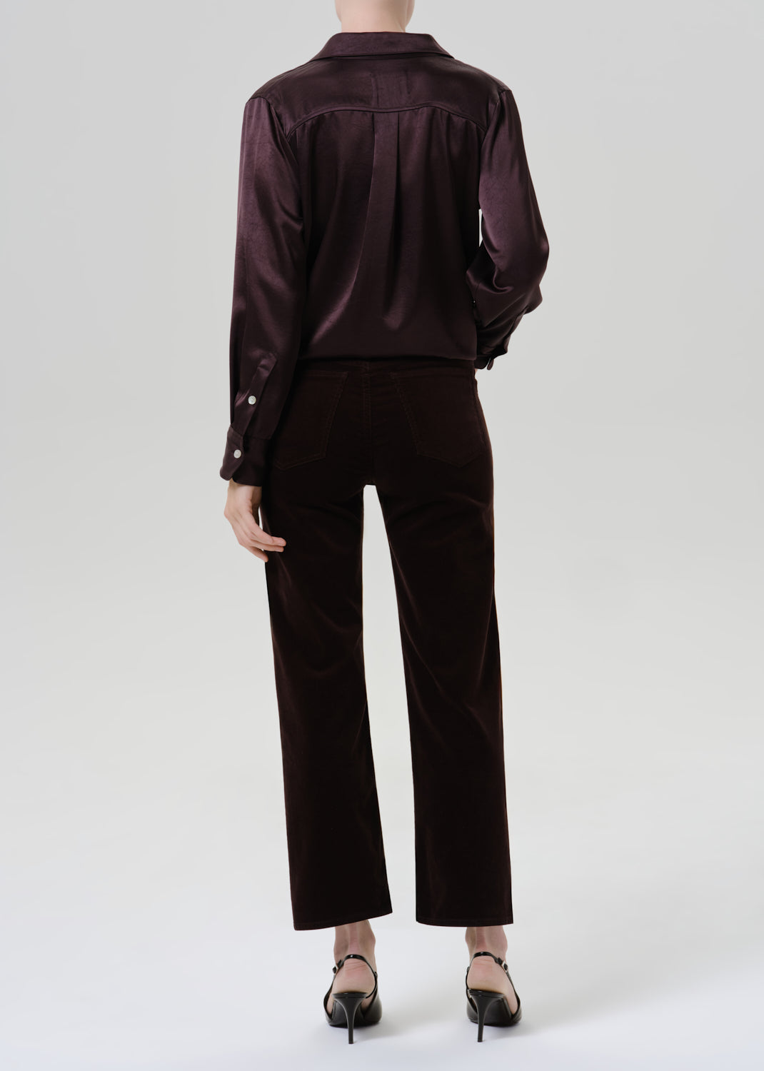 Person wearing burgundy button up shirt with black pants on a grey background