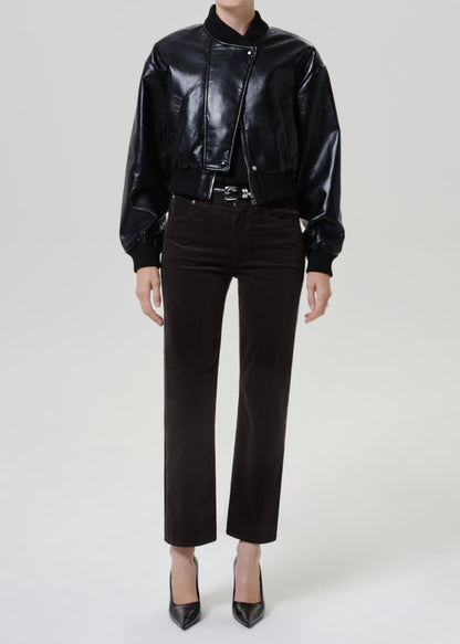A model wearing a black faux-leather bomber jacket, dark gray brown cropped trousers, and black pointed-toe heels, photographed against a light gray studio background.