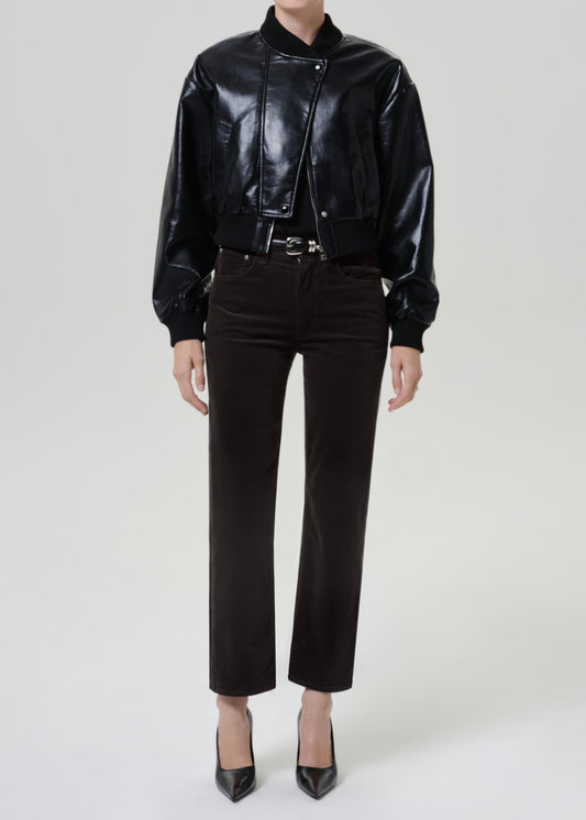 A model wearing a black faux-leather bomber jacket, dark gray brown cropped trousers, and black pointed-toe heels, photographed against a light gray studio background.