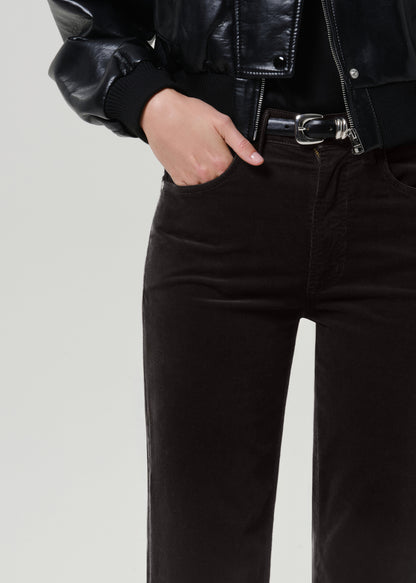 Close-up of a person wearing black leather jacket sleeves, a black belt with a silver buckle, and gray brown corduroy pants against a light gray studio background.