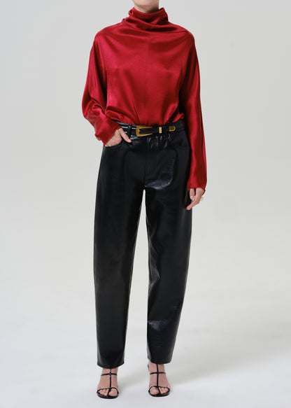 Woman wearing black leather pants with a red satin draped neck top on a grey background.