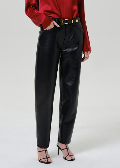 Woman wearing black leather pants with a red satin draped neck top on a grey background.