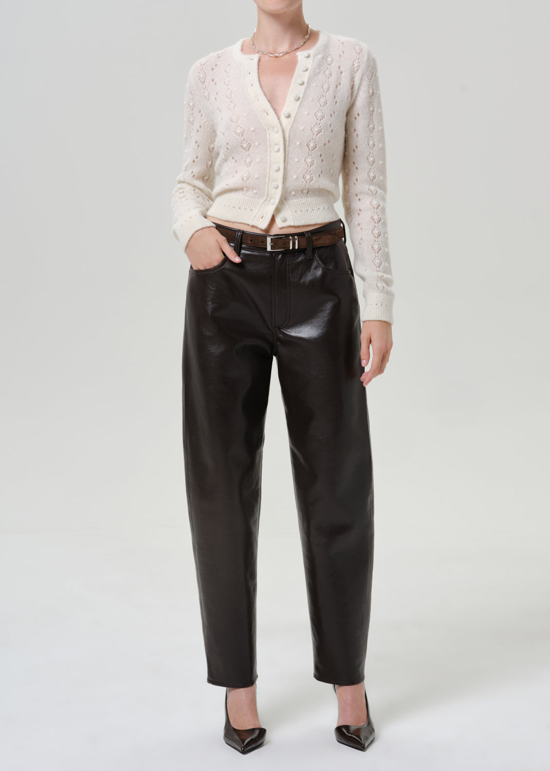 Woman wearing black leather pants with an ivory button-front cardigan on a grey background.