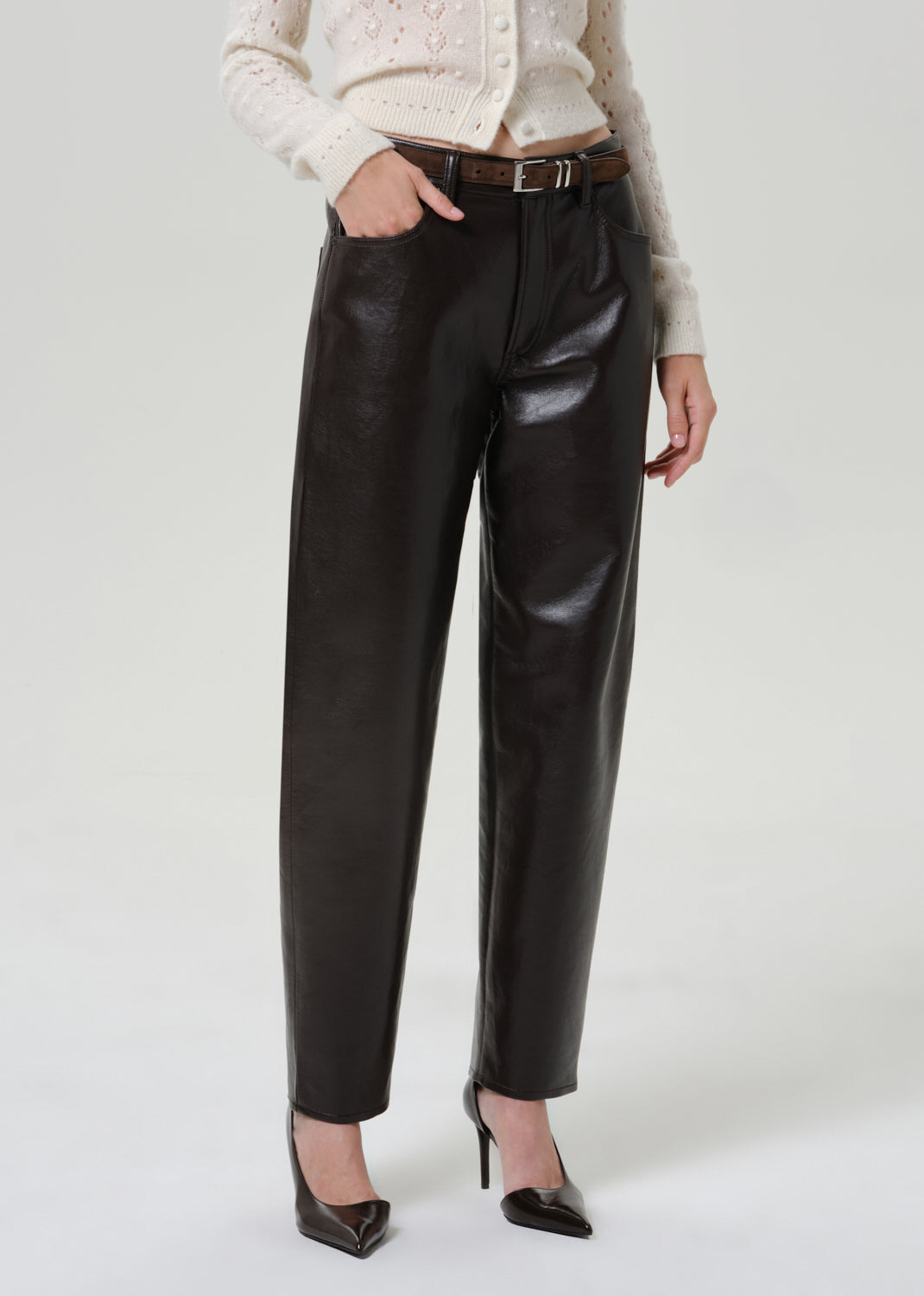 Woman wearing black leather pants with an ivory button-front cardigan on a grey background.