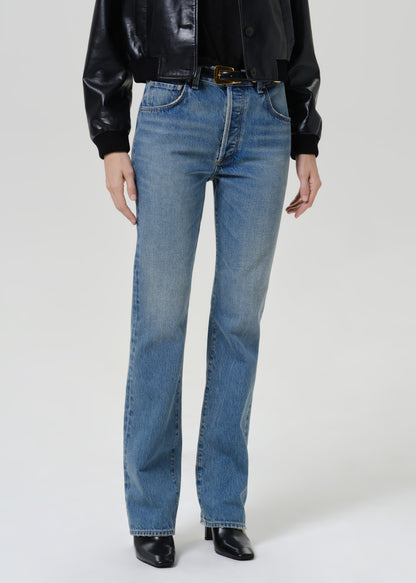 Woman wearing medium blue straight leg jeans with a black leather jacket on a grey background.